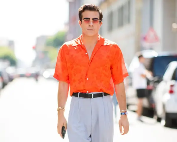 Hombre con camisa naranja estampada y pantalones grises, luciendo un elegante french tuck.