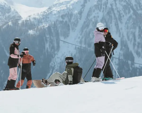 Grupa narciarzy i snowboardzistów odpoczywa na stoku, podziwiając majestatyczne góry Sierra Nevada.