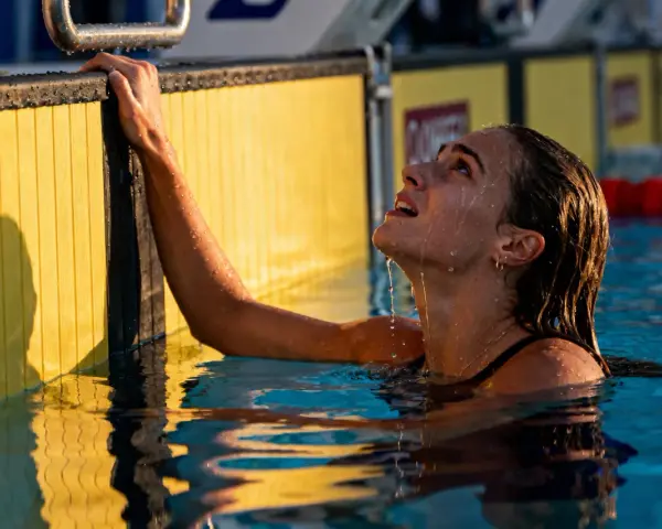 Nuotatrice con gocce d'acqua sul viso, aggrappata al bordo giallo della piscina. Si può fare il bagno in piscina con il ciclo, senza problemi.