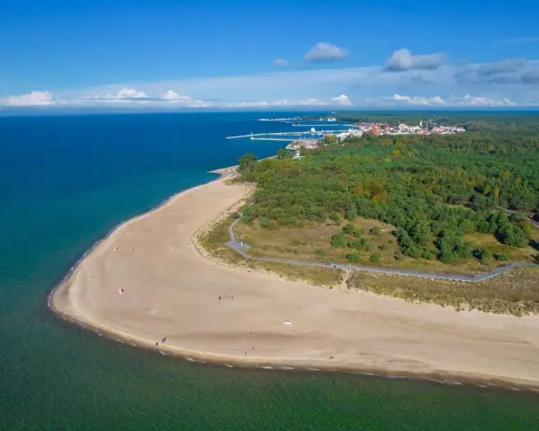 Piękna plaża i las sosnowy nad morzem. W oddali widać miasteczko i port. To właśnie tutaj jest Hel.