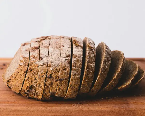 Pokrojony bochenek chleba razowego na desce. Zastanawiasz się, ile kalorii ma chleb razowy?