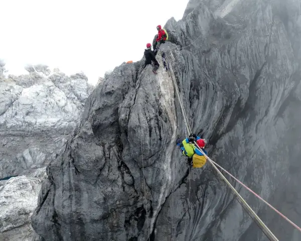 Wspinaczka na Piramidę Carstensza. Alpinista z plecakiem zjeżdża po linie, podczas gdy inni czekają na szczycie.