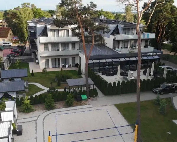 Nowoczesny hotel Cristal Spa z basenem i kortem do siatkówki plażowej, otoczony zielenią.