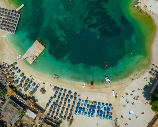 Widok z lotu ptaka na plażę w Albanii. Turkusowa woda, leżaki, parasole i łodzie. Idealne miejsce na albania wakacje 2026.