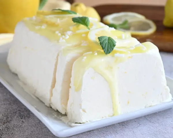 Un delizioso semifreddo al limone, guarnito con scorzette, menta e una glassa gialla brillante, pronto per essere gustato.