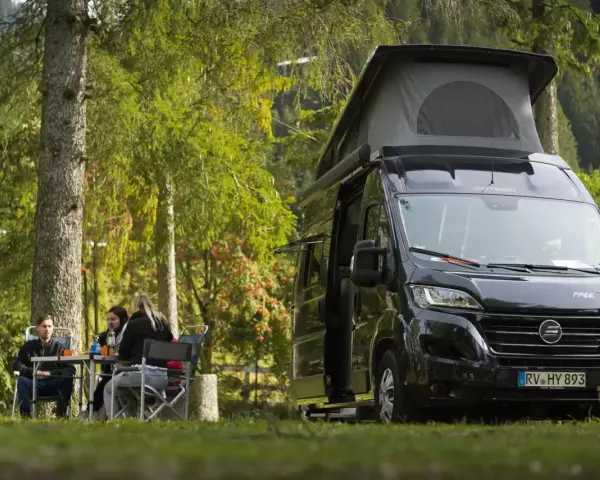 En solig dag med en clever sunny 540 husbil parkerad i skogen. Tre personer sitter vid ett bord och njuter av naturen.