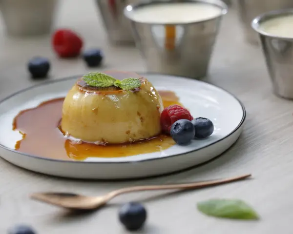 Delicioso flan de queso con caramelo, adornado con menta y frutos rojos.