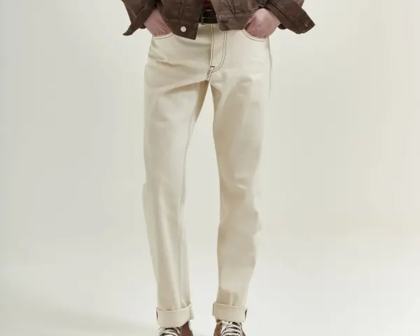 Uomo con giacca marrone e jeans chiari. La vestibilità è slim, non skinny, con risvolti alla caviglia.