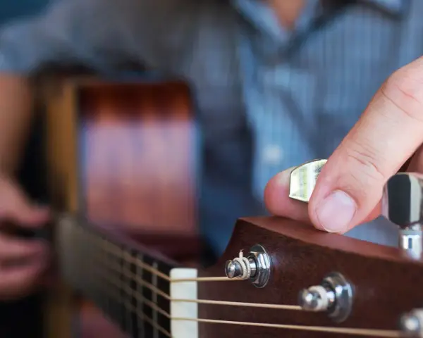 Dłoń stroi gitarę, kręcąc kluczem, by uzyskać idealny dźwięk E.