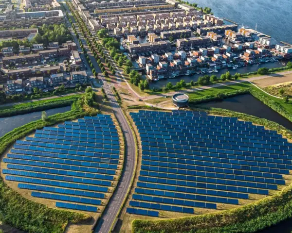 Un grande campo di pannelli solari, simbolo di rigenerazione urbana significato, circonda un quartiere residenziale con case moderne e canali.
