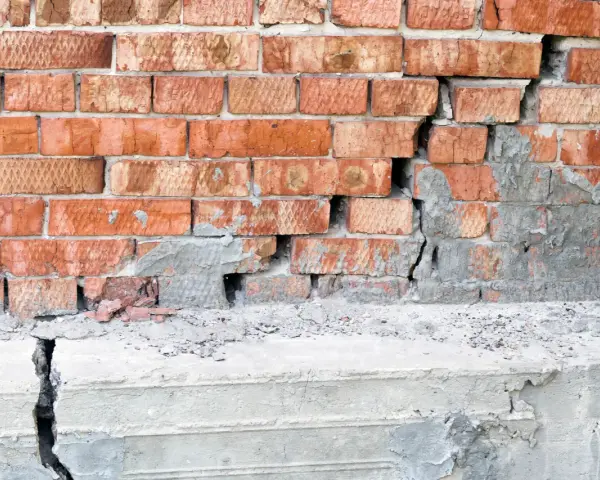 Pęknięta ceglana ściana i betonowy cokół, wskazujące na podbijanie fundamentów.