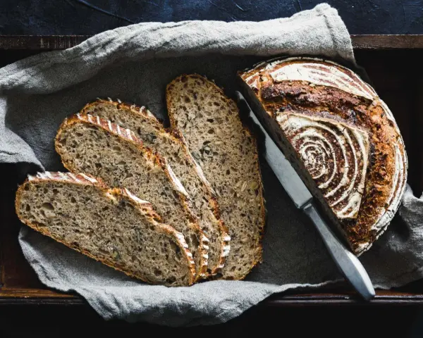 Ein rustikales Roggenbrot, in Scheiben geschnitten, liegt in einer Holzkiste auf Leinentuch. So vielseitig, was man aus Roggen machen kann!