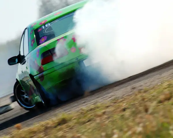 Zielony samochód z kwiatami driftuje, wydzielając dużo dymu.