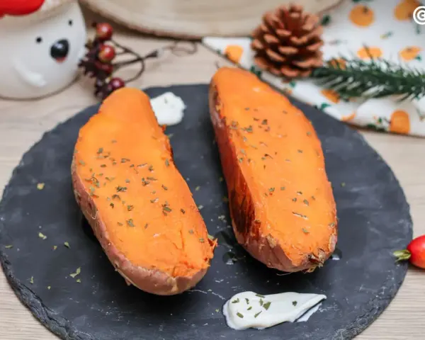 Dos mitades de boniato al horno, tiernas y doradas, con hierbas picadas y una cucharada de crema.