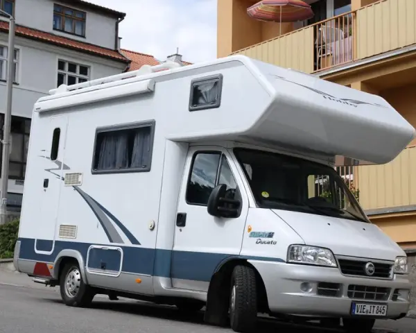 Biały kamper Fiat Ducato zaparkowany na ulicy. Zastanawiasz się, ile miejsc ma bus tego typu?