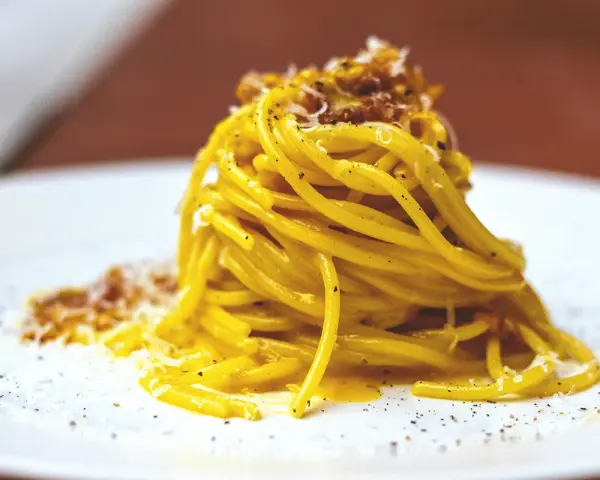 Un piatto di spaghetti alla carbonara fumante, guarnito con pecorino e pepe nero.