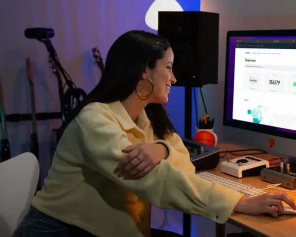 Junge Frau am Computer, die Statistiken für digitalen Musikvertrieb prüft. Gitarren im Hintergrund.