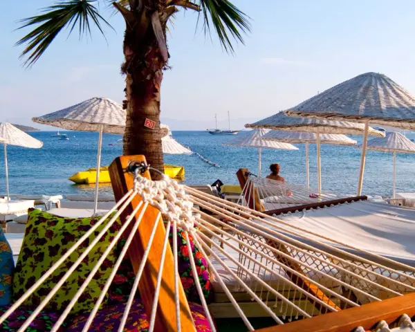 Hamaki i parasole na plaży w Turcji z widokiem na morze i żaglówki.