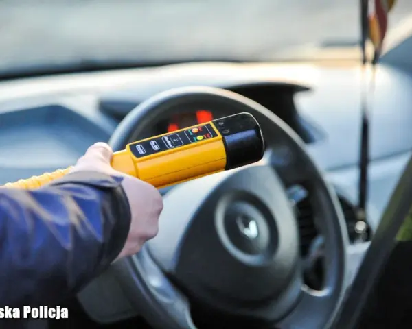 Policjant sprawdza, ile promili ma kierowca. Żółte światło na alkomacie sugeruje, że wynik jest poniżej dopuszczalnej normy.