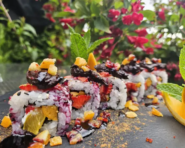 Roladki sushi z owocami, posypane cukrem pudrem i udekorowane miętą i pomarańczą.