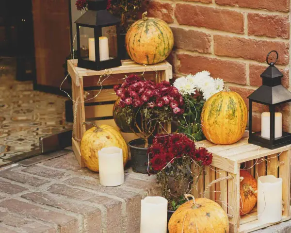 Gemütliche herbstdeko hauseingang mit Kürbissen, Laternen und Blumen auf Holzkisten.