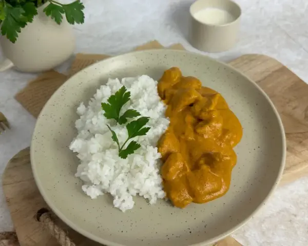 Pyszny Butter Chicken przepis na talerzu z ryżem i natką pietruszki. Idealny obiad.