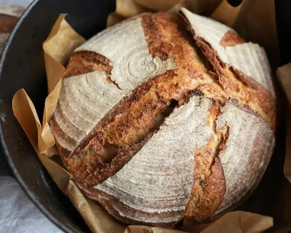 Ein frisch gebackenes Sauerteigbrot mit knuspriger Kruste liegt in einem Gusseisentopf. Perfekt für jedes Sauerteigbrot Rezept.