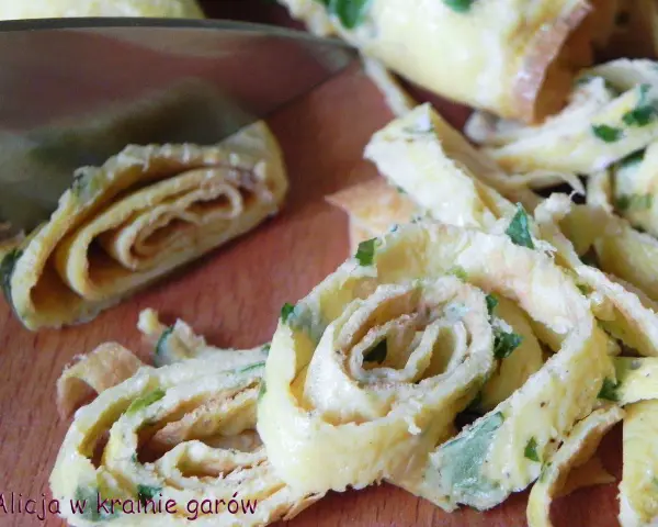 Roladki z jajek, idealne jako makaron keto z jajek, posypane szczypiorkiem, krojoną na desce.