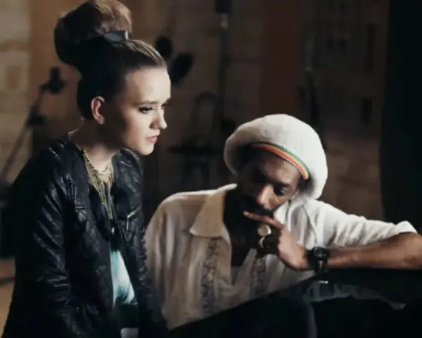 Snoop Dogg w białej koszuli i beretce Rasta, rozmawiający z młodą kobietą. Może to być scena z jednego z jego **snoop dogg utworów**.
