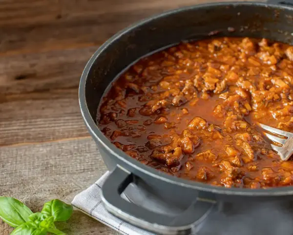Un saporito ragù di anatra, ricetta veneta, pronto in padella con una forchetta. Profumo di basilico fresco.