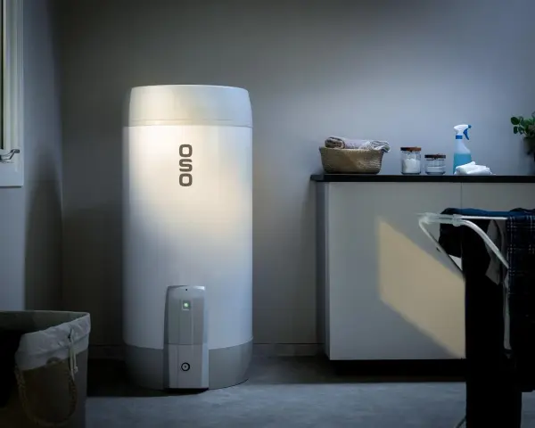 En OSO smart varmvattenberedare står i ett tvättstuga. Bredvid finns en tvättkorg och en torkställning med kläder.