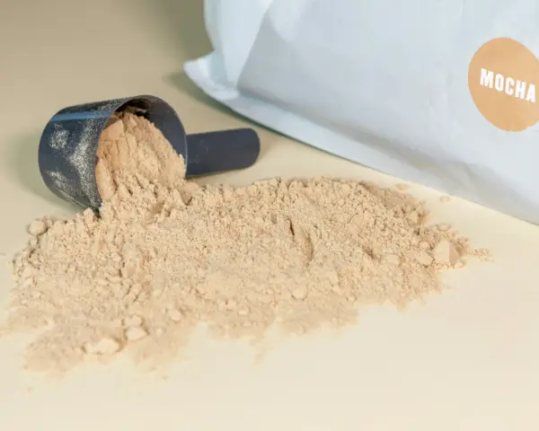 Moccha-smakande proteinpulver spillt från en skopa, med påsen i bakgrunden. Perfekt för att hålla koll på proteinpulver kcal.
