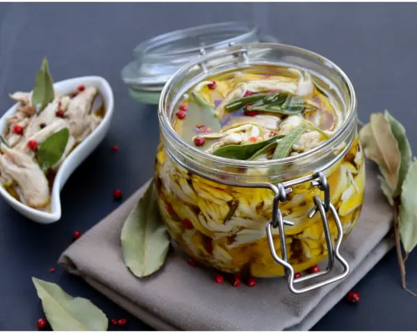 Tonno di coniglio sott'olio, sfilacciato e conservato in un barattolo di vetro con erbe aromatiche e pepe rosa.