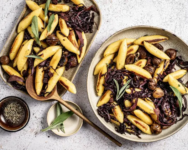 Schupfnudeln mit Rotkohl und Kastanien, garniert mit Salbei. Ein herzhaftes Gericht, das zum Genießen einlädt.