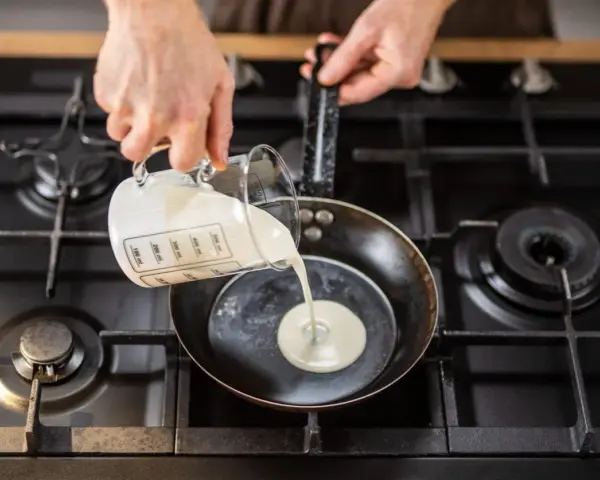 Mani versano panna da cucina in una padella su un fornello a gas.