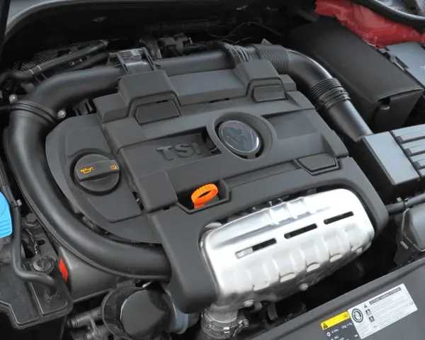 Silnik 1.4 TSI z widocznym logo VW. Widoczne elementy to m.in. pokrywa silnika, przewody, zbiornik płynu i filtr oleju.