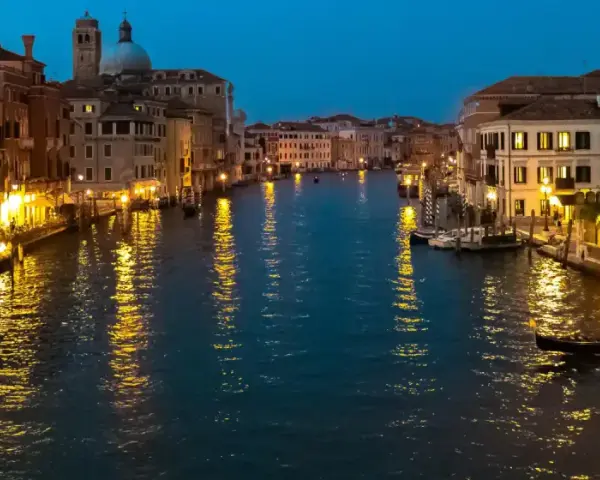 Serata magica per visitar Venezia: luci dorate sui palazzi e riflessi sull'acqua del Canal Grande, con gondole e ristoranti animati.
