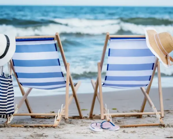 Dwa leżaki na plaży, gotowe na idealny weekend nad morzem. W tle szum fal i błękitne niebo.