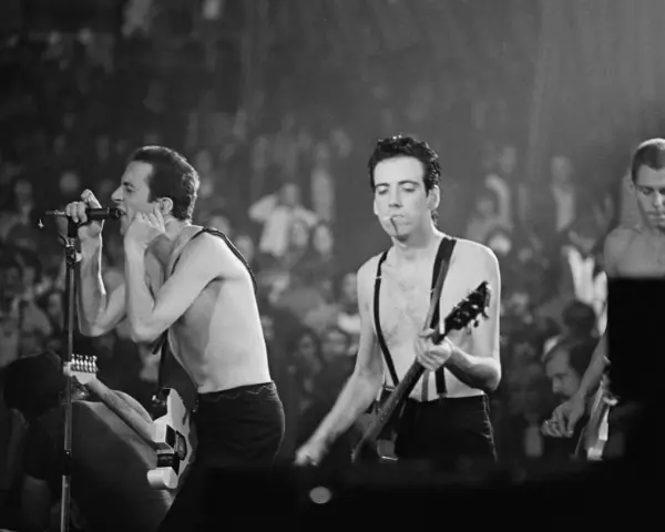 Le chanteur de The Clash, Joe Strummer, chante avec passion devant une foule en délire, guitare à la main.