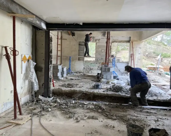 Travaux de démolition en cours pour une aide à la rénovation maison ancienne. Des ouvriers utilisent des outils pour casser le béton.