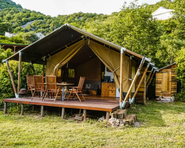 Glamping w Czarnogórze: namiot z drewnianym tarasem, stołem i krzesłami, otoczony zielenią. Idealne miejsce na relaks.