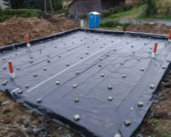 Fundament budowlany z folią i rurami. Widać małe kostki, które służą jako dystanse do zbrojenia, zapewniając odpowiednią grubość otuliny betonu.