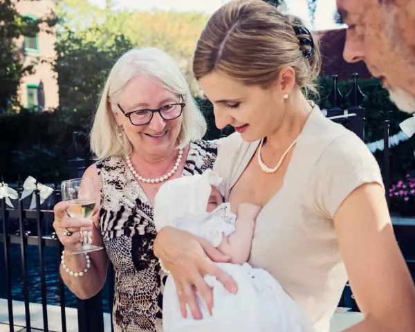 Elegancka mama karmi dziecko na chrzcinach. Babcia z kieliszkiem wina podziwia wnuka. Jak się ubrać na chrzciny? Klasycznie i z klasą.