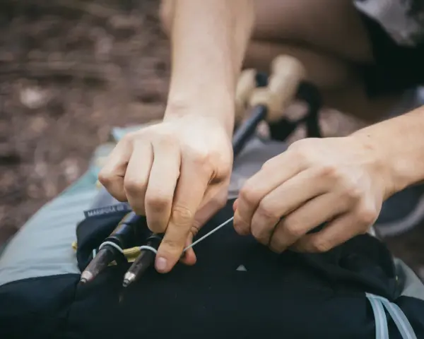 Ręce zapinają kijki trekkingowe do plecaka. Prosty sposób, jak przypiąć kijki do plecaka, by były zawsze pod ręką.