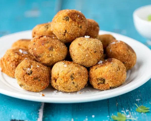 Pile di polpette tonno e ricotta dorate e croccanti, cosparse di sale grosso, su un piatto bianco.