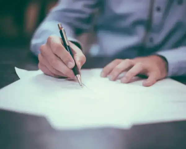 Dłoń pisze długopisem na papierze, finalizując wpis do księgi wieczystej.