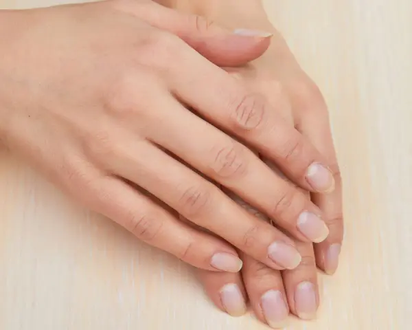 Mani curate, con unghie naturali e sane che sembrano respirare. La pelle è liscia e luminosa, poggiata su una superficie chiara.