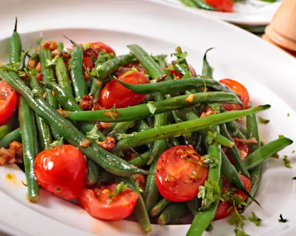 Insalata di fagiolini freschi con pomodorini ciliegino e erbe aromatiche, servita in un piatto bianco.