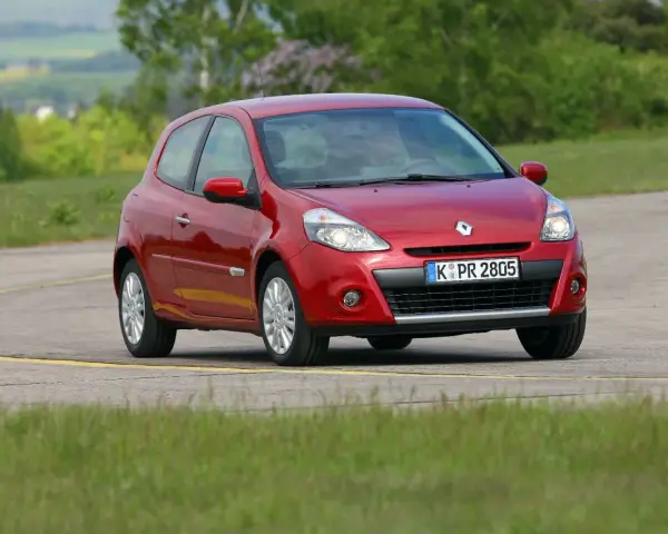 Czerwony Clio 3 na zakręcie drogi, otoczony zielenią.