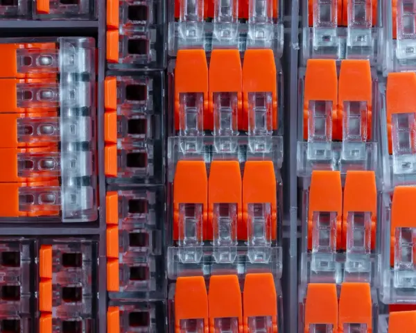 Zbliżenie na pomarańczowe złącza elektryczne w przezroczystych obudowach, ułożone w rzędy.